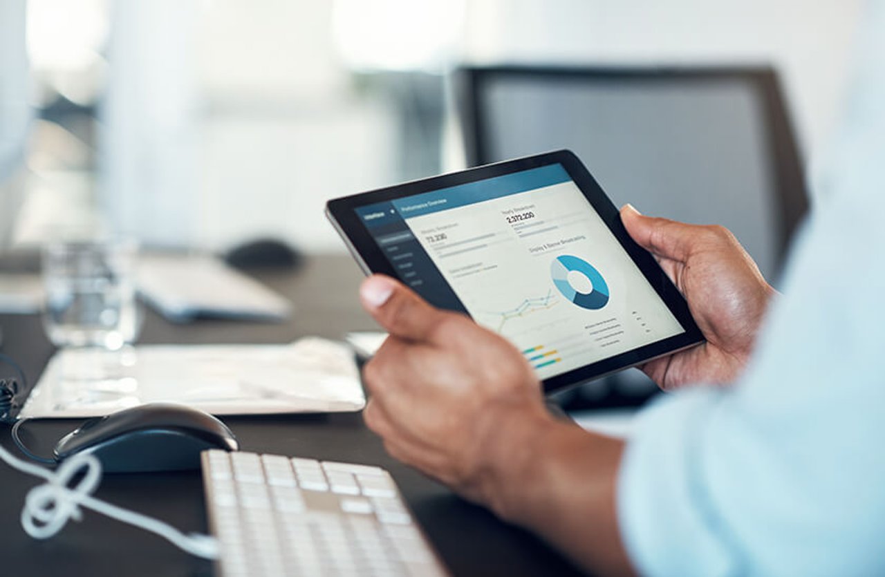 person holding tablet with financial information on the screen at desk