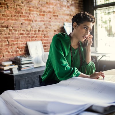 Stock photo of woman, a small business owner who is on her cell phone and typing notes into her laptop.