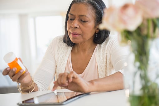 older woman holding prescription bottle and looking at tablet