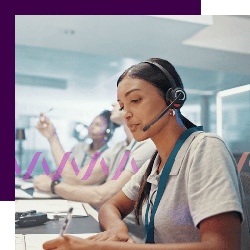 Photo of several contact center employees sitting side by side. The woman in the foreground is wearing a headset and writing something on a notepad.