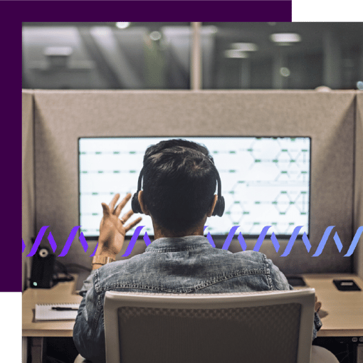 Photo of a call center agent taken from behind. Over his shoulder on the monitor screen can be seen an ongoing customer interaction. A series of small purple waveforms runs across the frame.