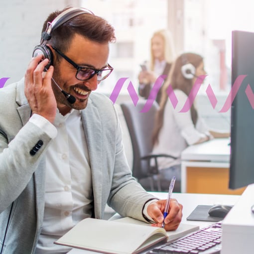 Photo of a smiling call center agent talking to a customer through his headset and writing notes