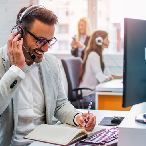 Photo of a smiling call center agent talking on the phone to a customer and taking notes.