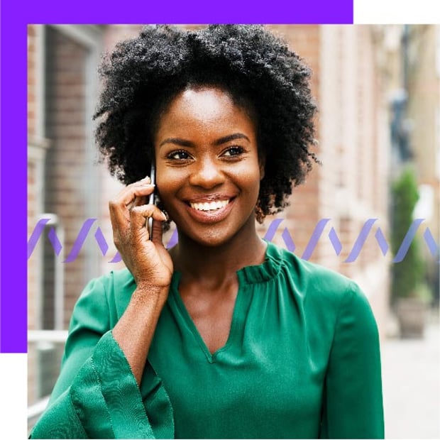 Photo of a smiling woman outdoors in a city setting talking into a cell phone.
