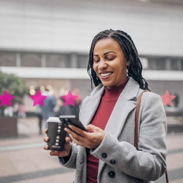 Photo of a woman holding a mobile phone and smiling at the screen; she has a coffee cup in her other hand; the photo has pink stars added to the background to imply communications trends