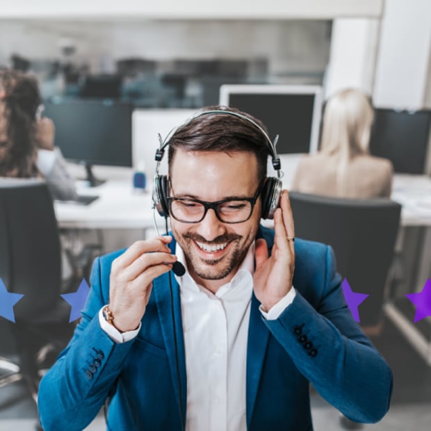 Image of a man seated at a desk, talking into a headset, and smiling