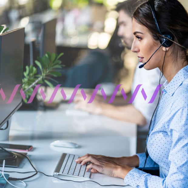 UC Call Center Campaigns Blog Header Photo of agents working in a call center. In the foreground, a woman is typing on her computer while talking to a customer on her headset. In the background, a series of small purple waves runs across the frame.