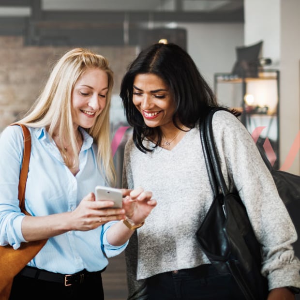 Generative AI for retail image Photo illustration of two women; the woman on the left is holding her mobile phone and pointing at an image on the screen to show the woman on the right
