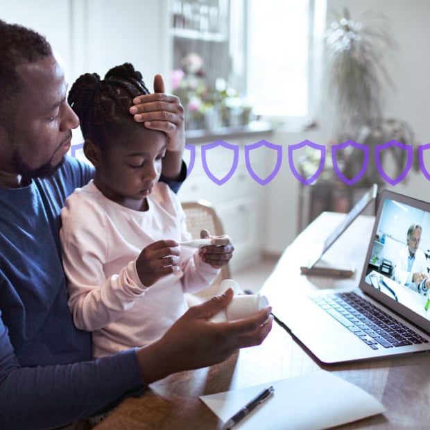 HIPAA compliant telehealth blog header Photoillustration of a man with his daughter sitting in his lap; the man is feeling his daughter's forehead and she is holding a thermometer indicating she is ill; the man and child are seated facing a laptop and a doctor is on the screen in his office