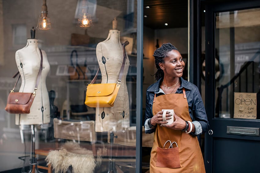 business owner standing outside fashion shop holding cup of coffee