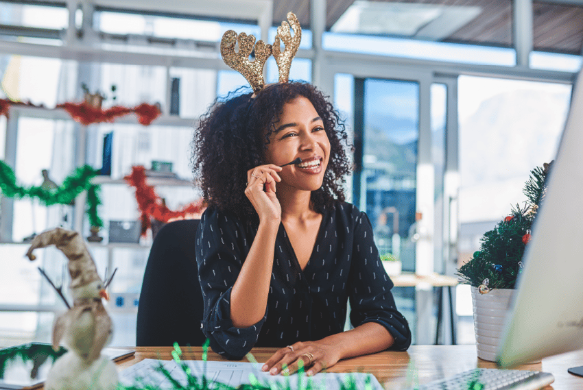 Holiday and Peak Season Shopping Photo of a woman sitting in front of a computer. She is smiling and is wearing a phone headset.