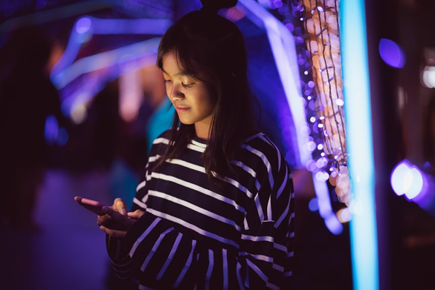 Photo of a woman standing outdoors, holding and texting on her phone