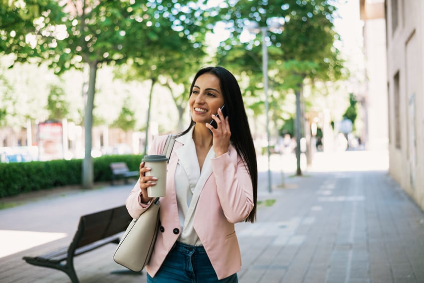UC Is VoIP Reliable Article Header Photo of smiling woman outdoors away from the office on her cell phone.