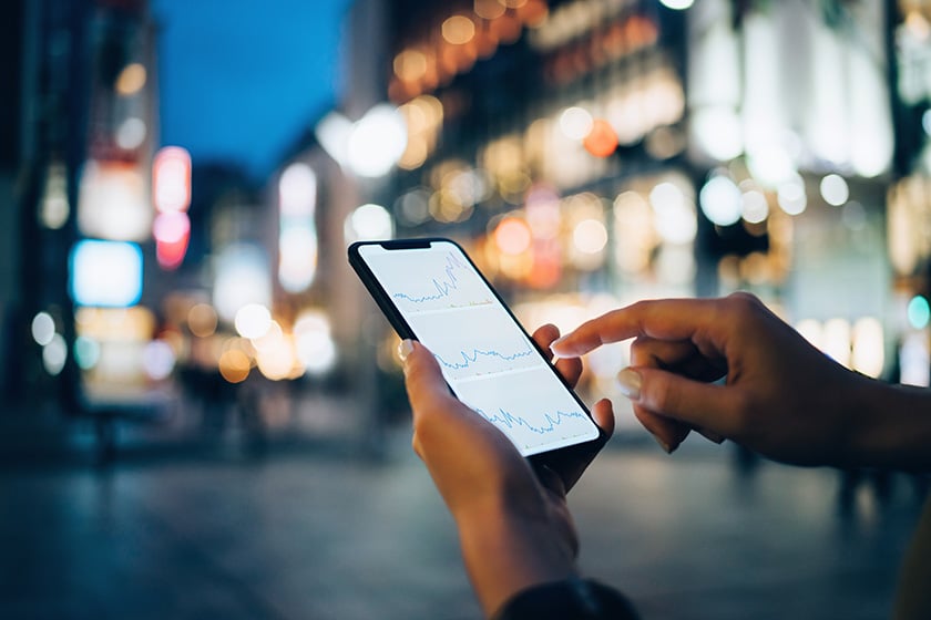 Innovative financial services companies are using communications APIs to transform the customer experience, delighting sometimes tentative customers with real-time authentication, video, voice, and messaging interactions. Businesswoman reading financial trading data on smartphone in downtown city street against illuminated urban skyscrapers