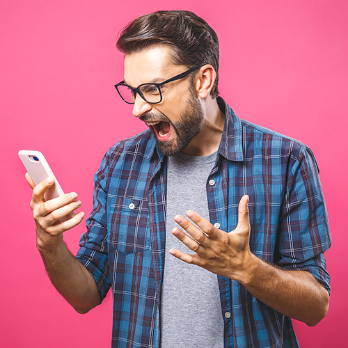 Photo of angry man holding his cellphone. He is looking at the screen and screaming in frustration.