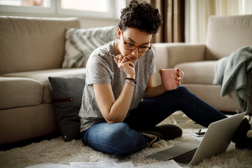 woman at home looking at finances on paper and laptop 